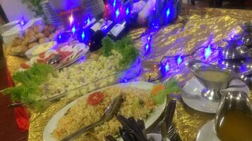 Een buffet met diverse gerechten, zoals rijst, salades en brood, op een gouden tafelkleed met blauwe decoratieve verlichting.