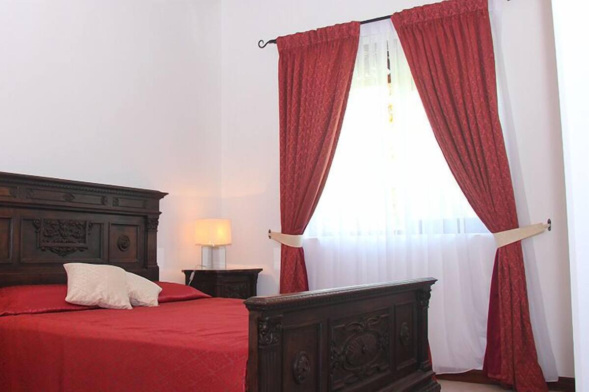 A bedroom with a wooden bed, red curtains, and two bedside lamps.