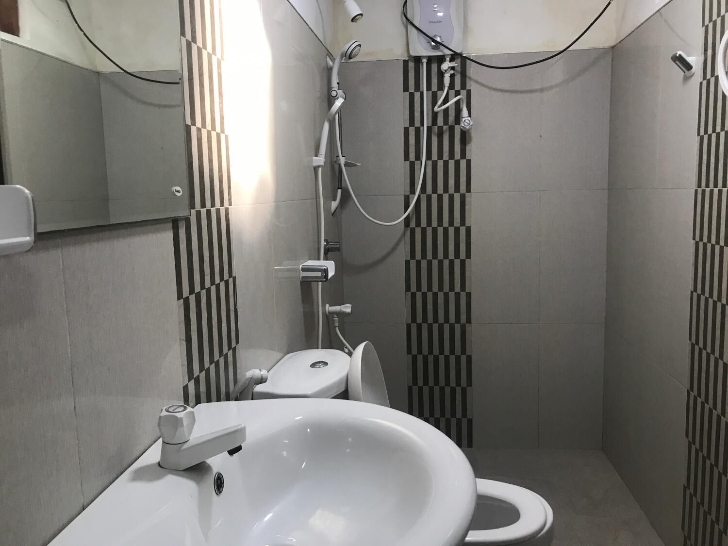 Un baño pequeño con inodoro, lavamanos y ducha. Las paredes presentan un patrón de baldosas a rayas.