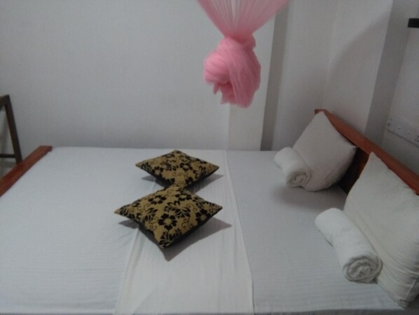 A neatly made bed with white and patterned pillows, a wooden headboard, and a white wall.