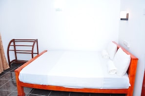 Una cama bien hecha con sábanas y almohadas blancas, un cabecero de madera y una pequeña silla de madera.