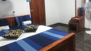 A bedroom with a bed, wooden headboard, blue and white bedding, a wooden door, a mirror, and a standing fan. - Hotel Camorich (Thissamaharama)