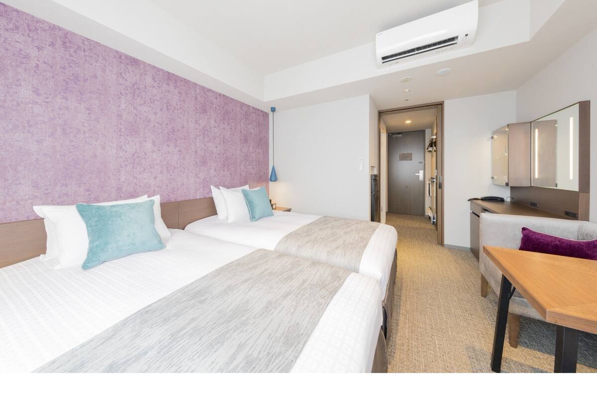Ein Hotelzimmer mit zwei Betten, einem Schreibtisch, einem Stuhl, einer Klimaanlage und einem Spiegel.