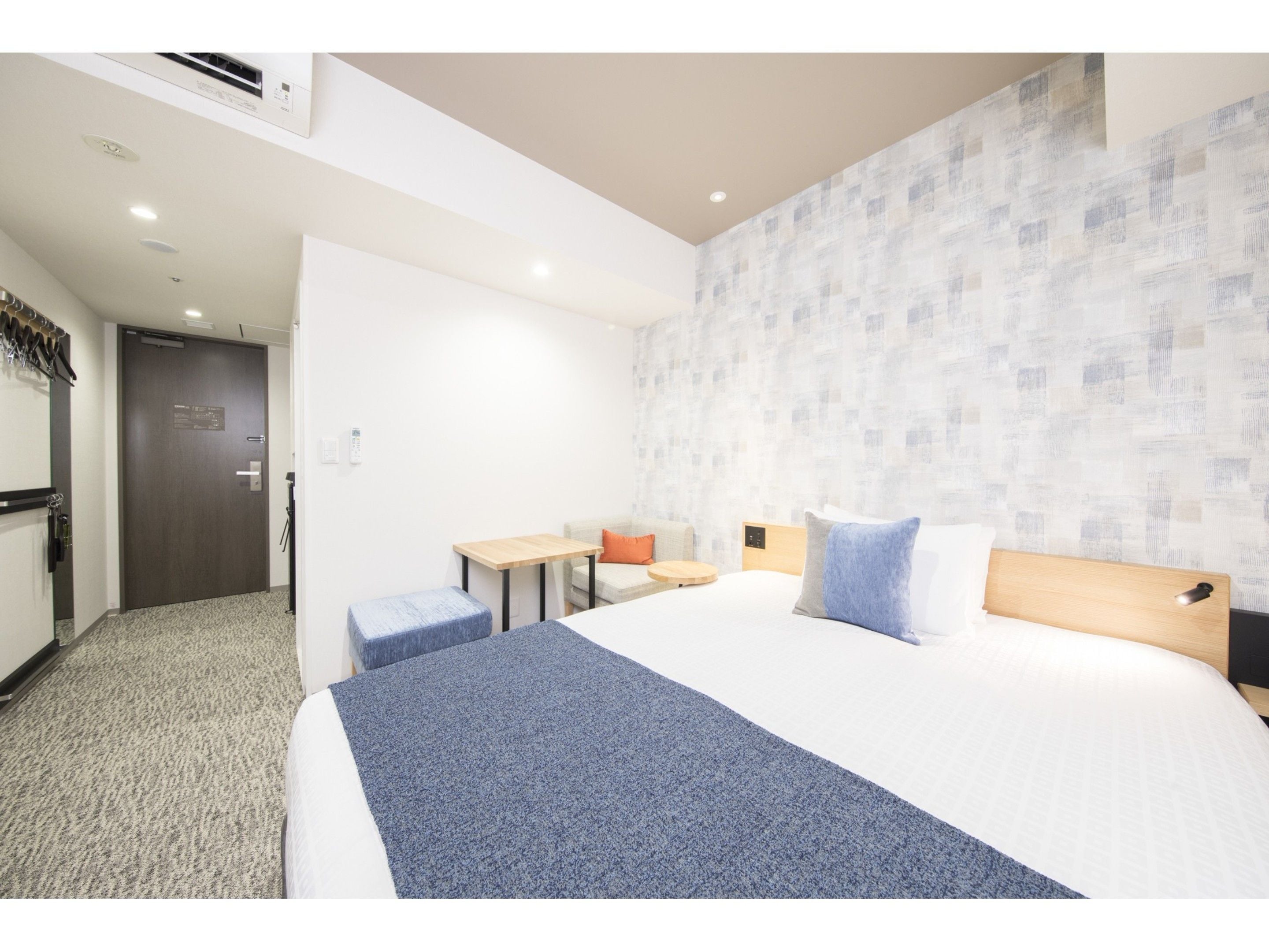 A hotel room with a bed, a desk, a chair, and a small table.