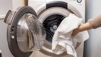 A front-loading washing machine with a transparent door, a control panel with various buttons, and a white towel hanging on the door.