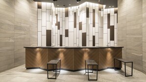Un espace d’accueil au design moderne, comprenant un comptoir d’accueil incurvé, deux tabourets en métal noir et un mur orné de motifs géométriques.