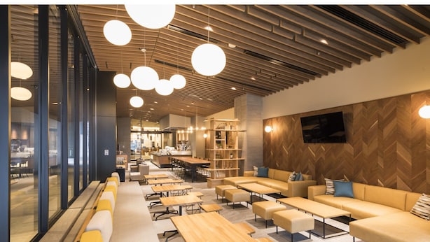 Un café moderne avec des tables en bois, des sièges rembourrés de couleur jaune et des luminaires suspendus.