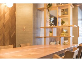 Un comedor moderno con una mesa de madera larga y sillas, una pared con motivo de espiga, y una unidad de estanterías de madera con objetos decorativos.