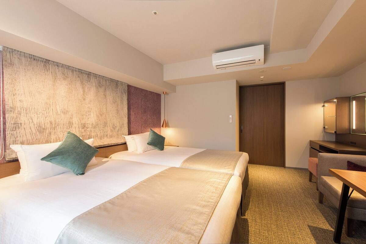 Ein Hotelzimmer mit zwei Betten, einem Schreibtisch, einem Stuhl, einer Klimaanlage und einem Spiegel.