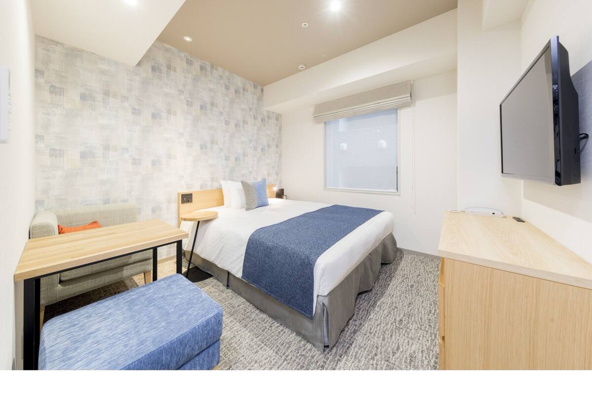 Ein modernes Hotelzimmer mit Bett, Schreibtisch, Stuhl, Fernseher und Fenster.