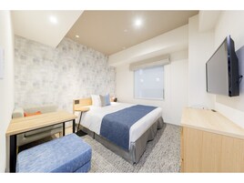 A modern hotel room with a bed, a desk, a chair, a TV, and a window.