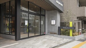 Un bâtiment moderne avec une façade en verre, une enseigne indiquant « TOKYU STAY » et une autre, sur le mur, indiquant « SIMPLE CAFE ».