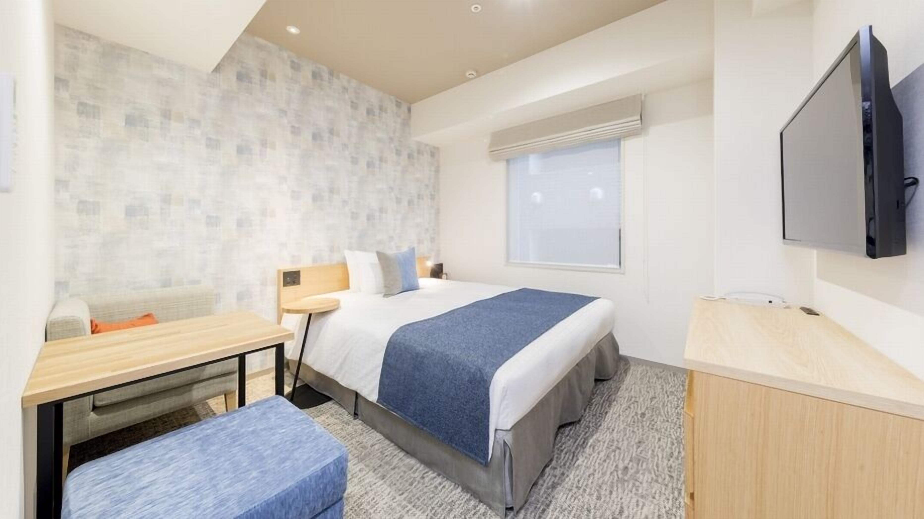 Une chambre d’hôtel avec un lit, un bureau, une chaise, une télévision et une fenêtre.