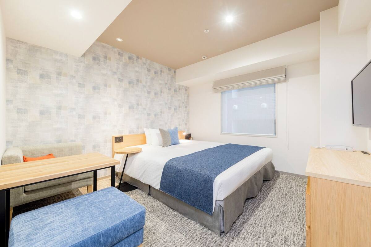 Ein Hotelzimmer mit Bett, Schreibtisch, Stuhl, Fernseher und Fenster.