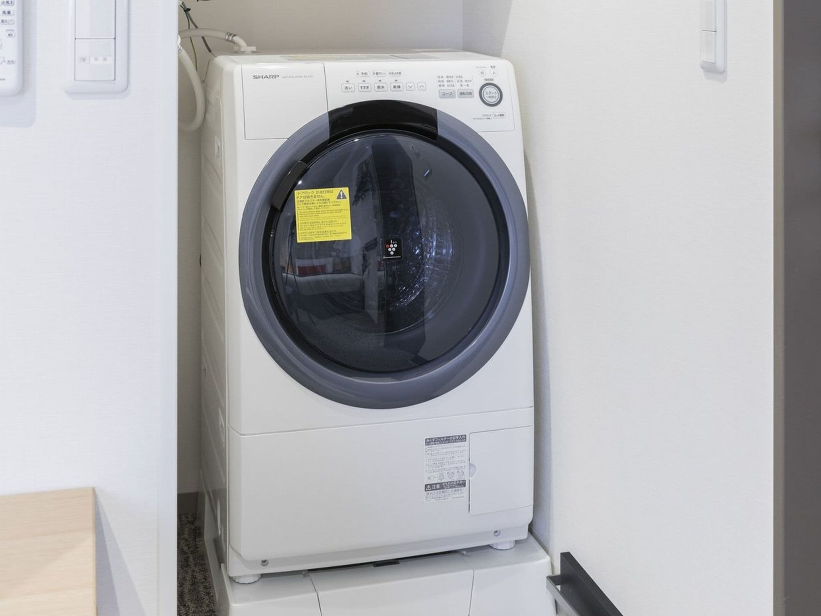 A front view of a white washing machine with a control panel and a yellow warning label.