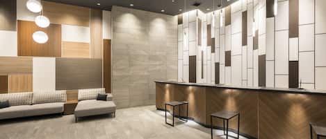 A modern reception area with a wooden reception desk, a sofa, and two small tables.