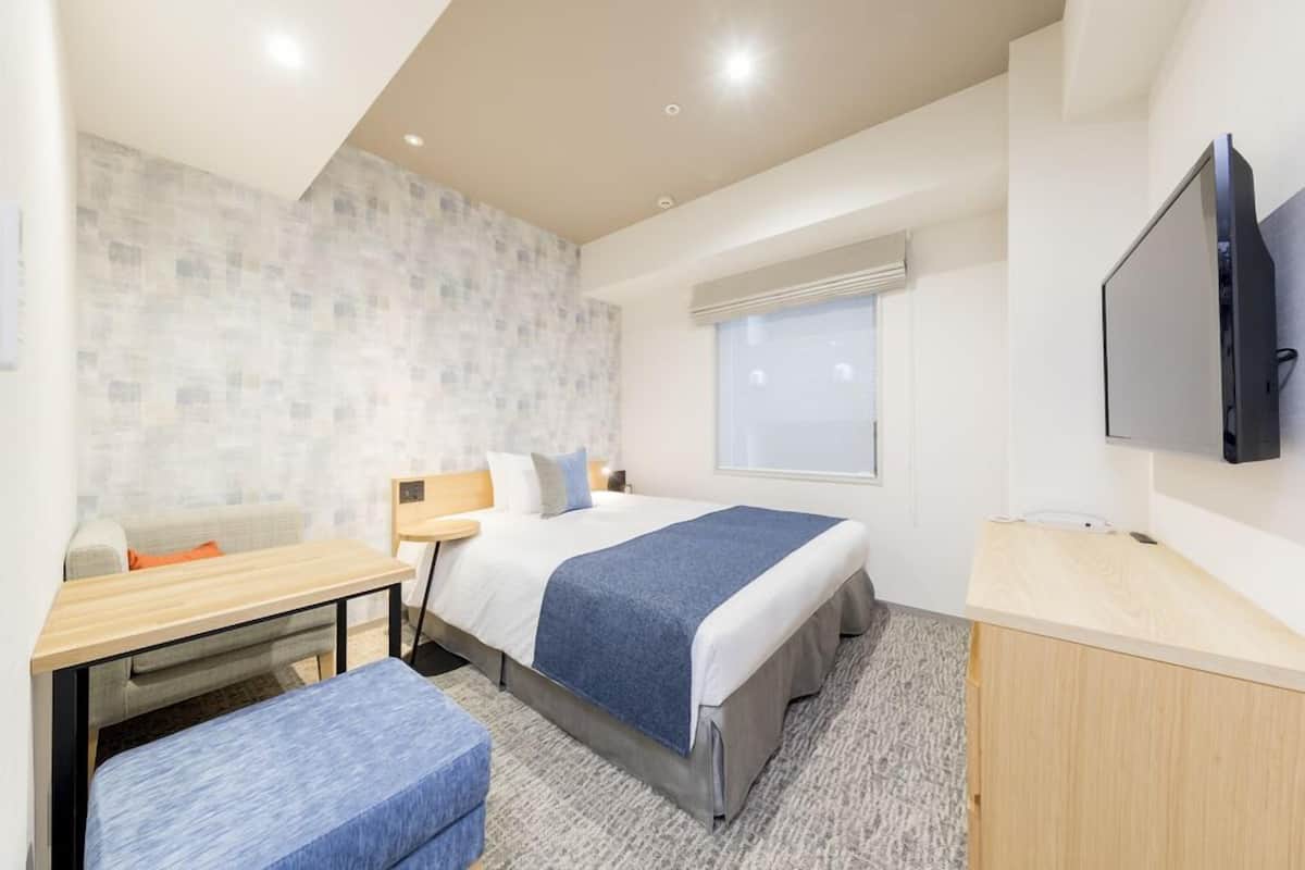 Una habitación de hotel moderna con cama, escritorio, televisor y ventana.