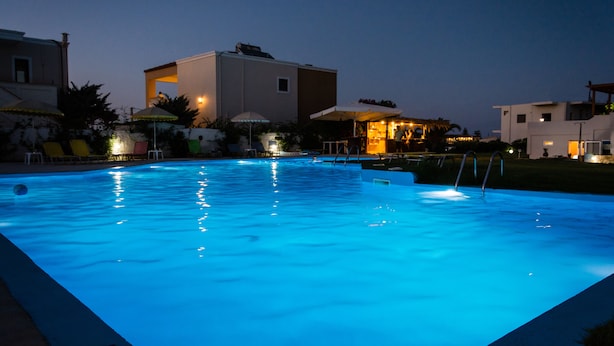 A swimming pool at dusk with surrounding buildings and umbrellas. - Nereides Hotel (Platanias)