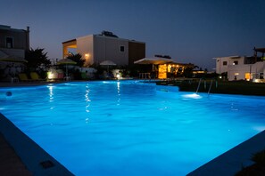 A swimming pool at dusk with surrounding buildings and umbrellas. - Nereides Hotel (Platanias)