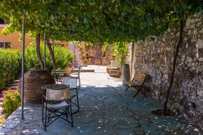 An outdoor patio with stone flooring, a wooden bench, and a table with chairs. - Archontiko Maisonettes (Zakynthos)