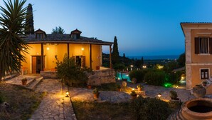 Una villa con un camino de piedra que conduce a una piscina, rodeada de plantas en macetas y vistas al mar.