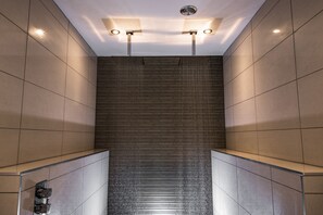Un área de ducha moderna con pared y techo revestidos de azulejos, e iluminación empotrada.