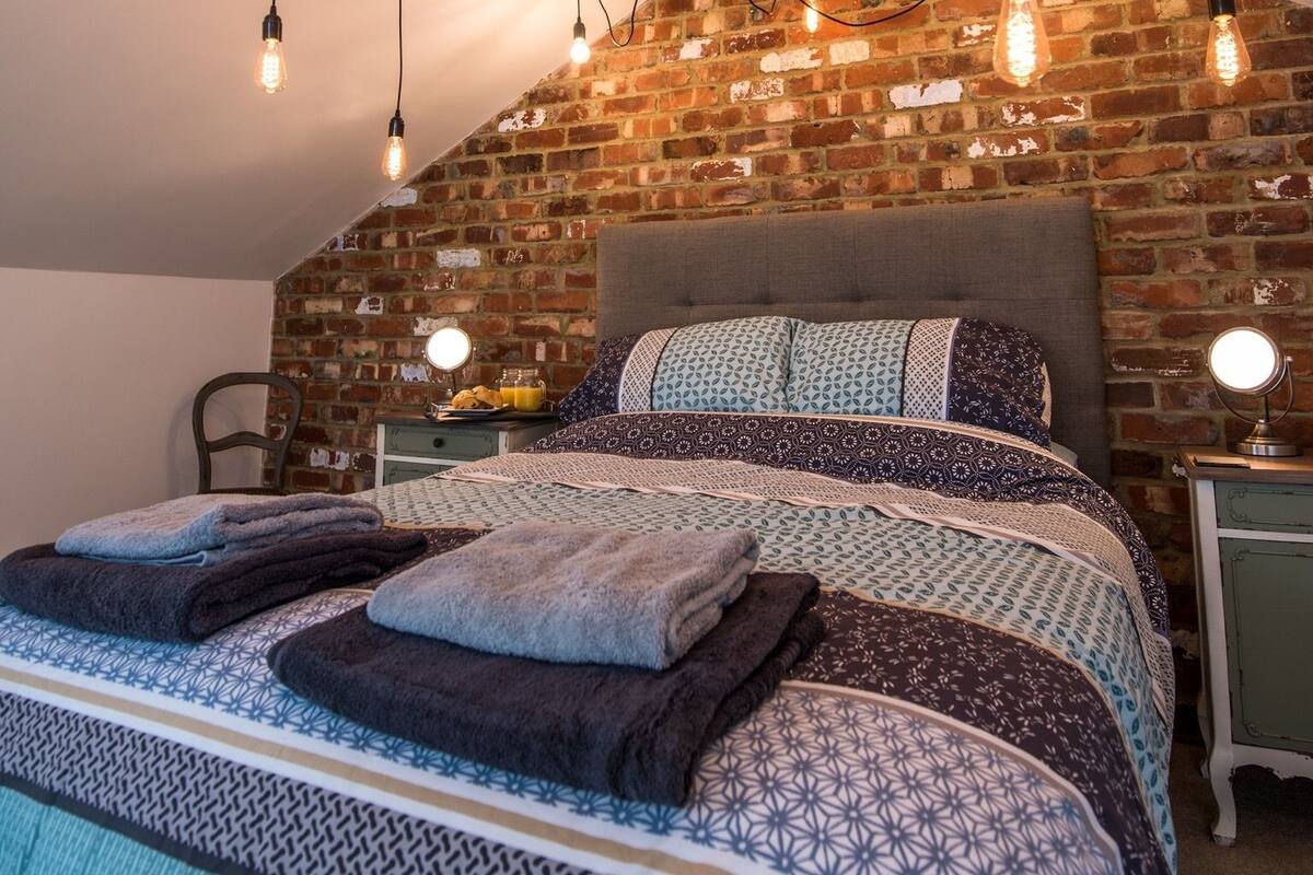 Une chambre avec un mur en briques, un lit recouvert d’une literie à motifs et plusieurs lampes suspendues.