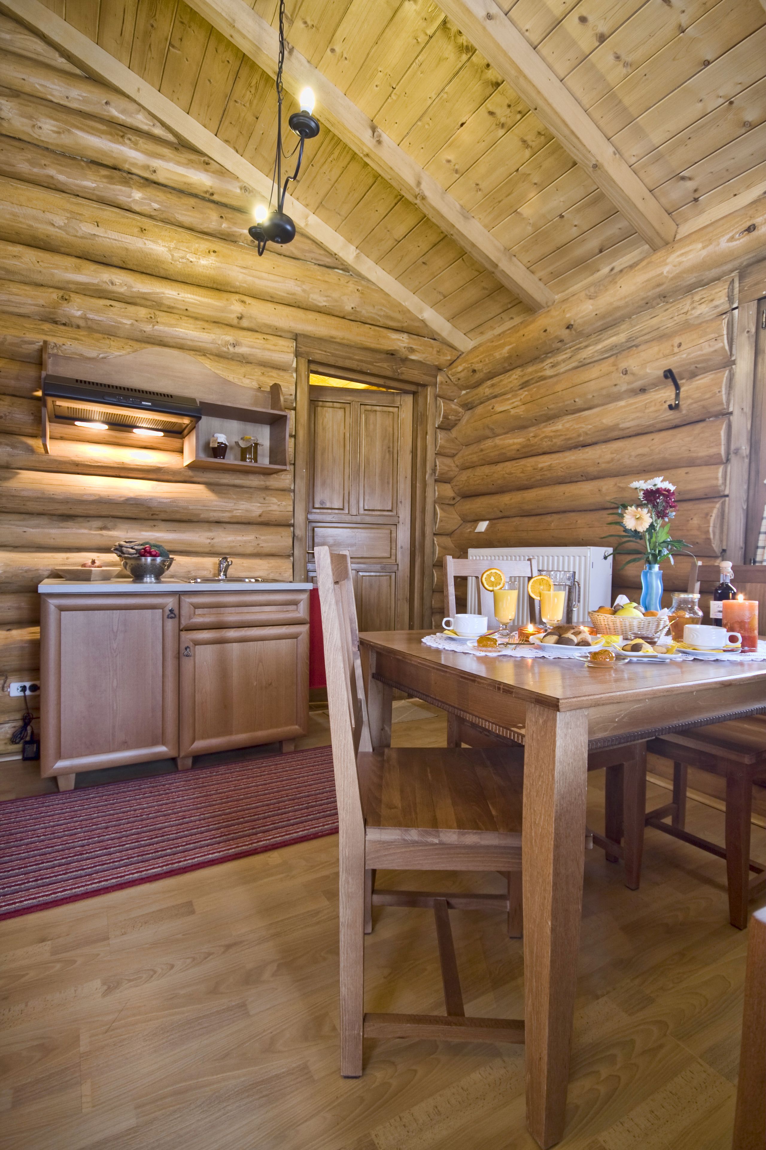 A wooden interior with a dining table set for breakfast, wooden cabinets, and a hanging light fixture.