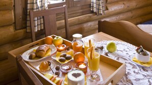 A wooden cabin interior with a breakfast tray on a table, plaid curtains, and a window with a view.