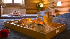 A cozy log cabin room with a wooden bed, a bedside table with a lamp, and a breakfast tray with eggs, toast, and juice.