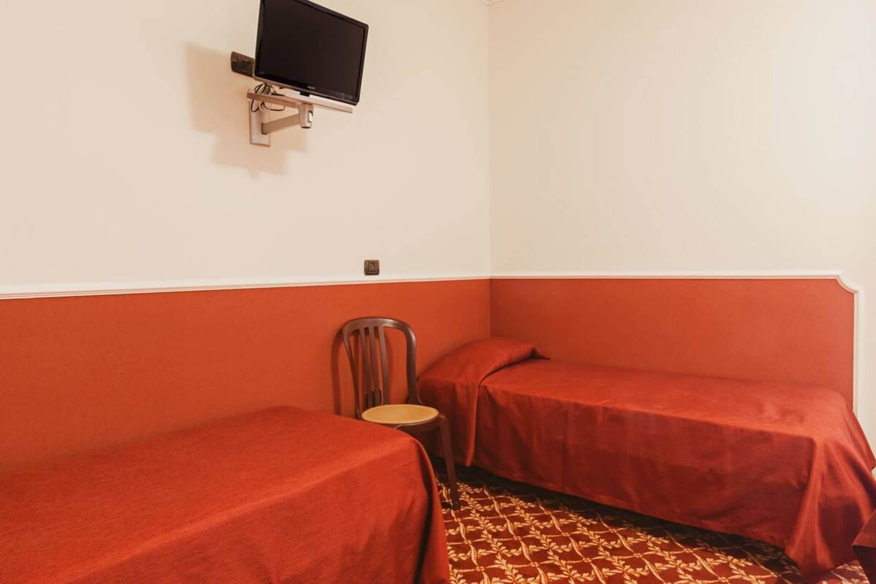Une chambre avec deux lits simples, une chaise, un téléviseur fixé au mur et une moquette à motifs.