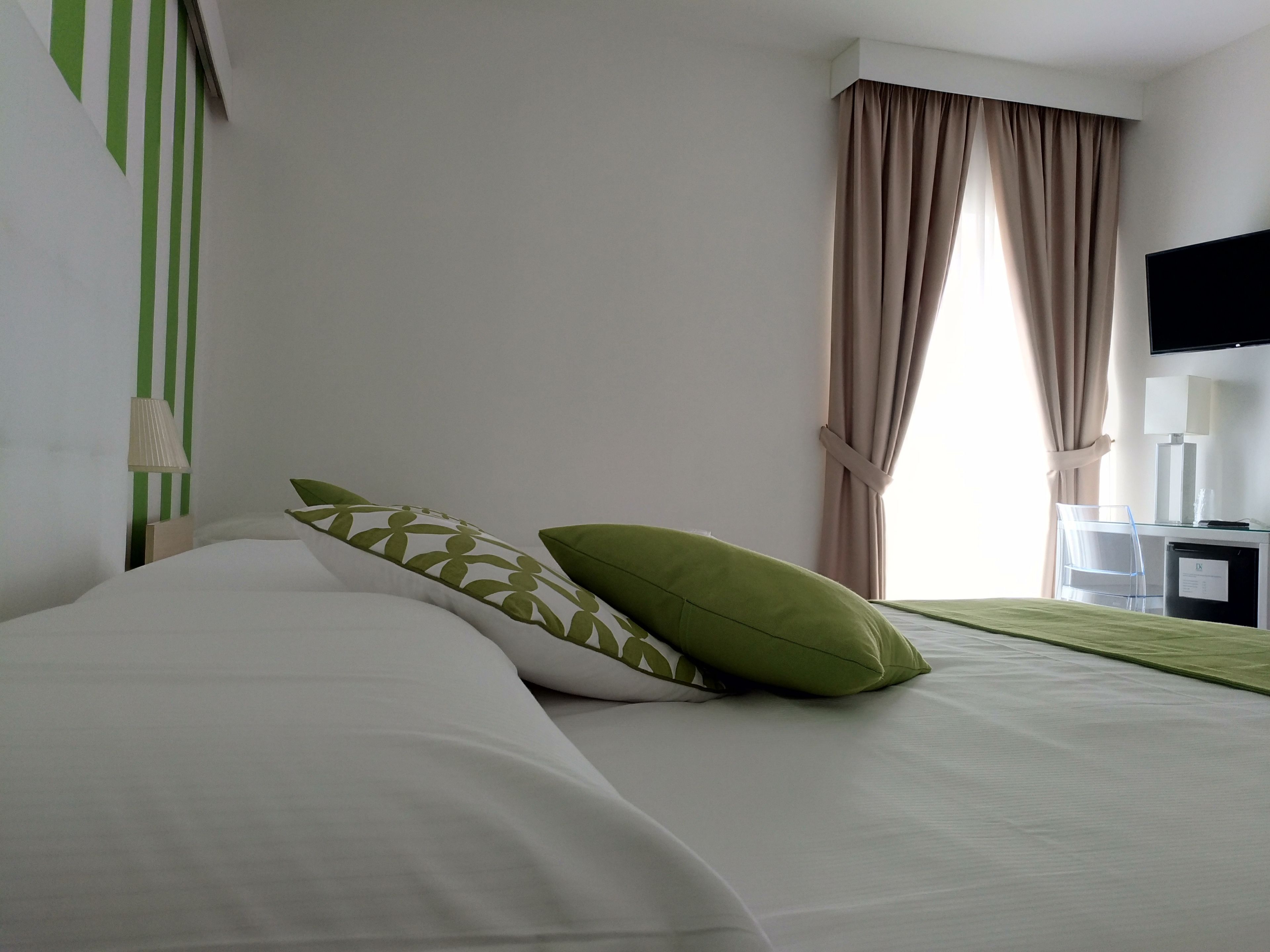 Una habitación de hotel con cama, escritorio, televisor y ventana con cortinas.