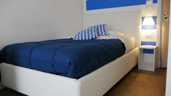 A bed with a blue and white patterned pillow, a white headboard, and a bedside table with a lamp.