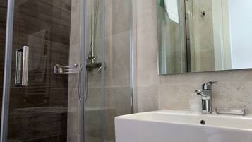 Une salle de bain moderne avec une douche à parois de verre, un lavabo blanc et un grand miroir au-dessus du lavabo.