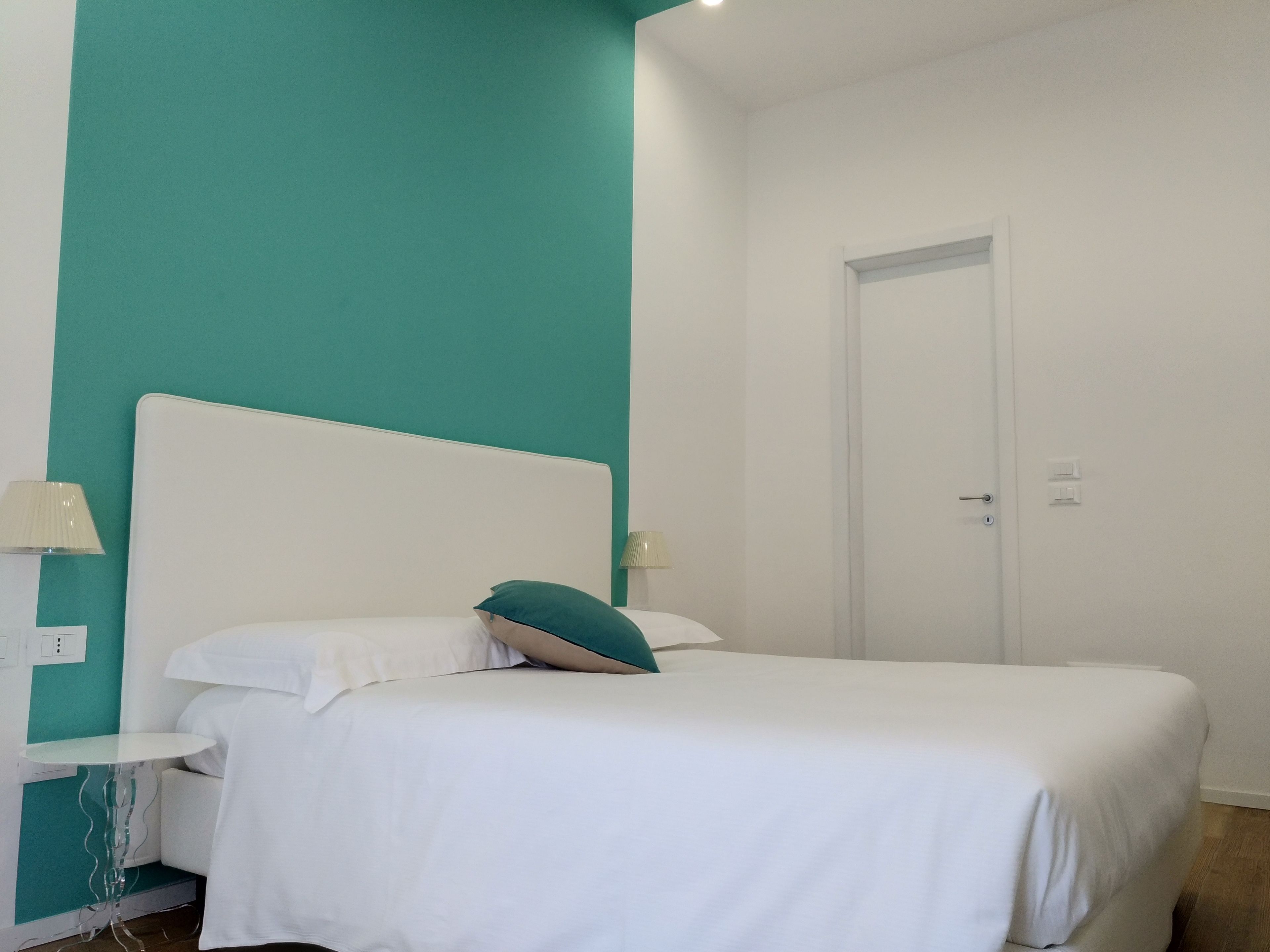 A bedroom with a white bed, teal accent walls, and a white door.