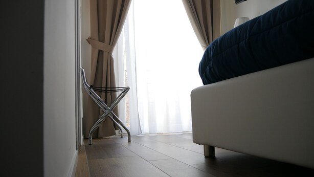 A bedroom with a bed, a chair, and a window with curtains. - Domus Nova (Reggio Calabria)
