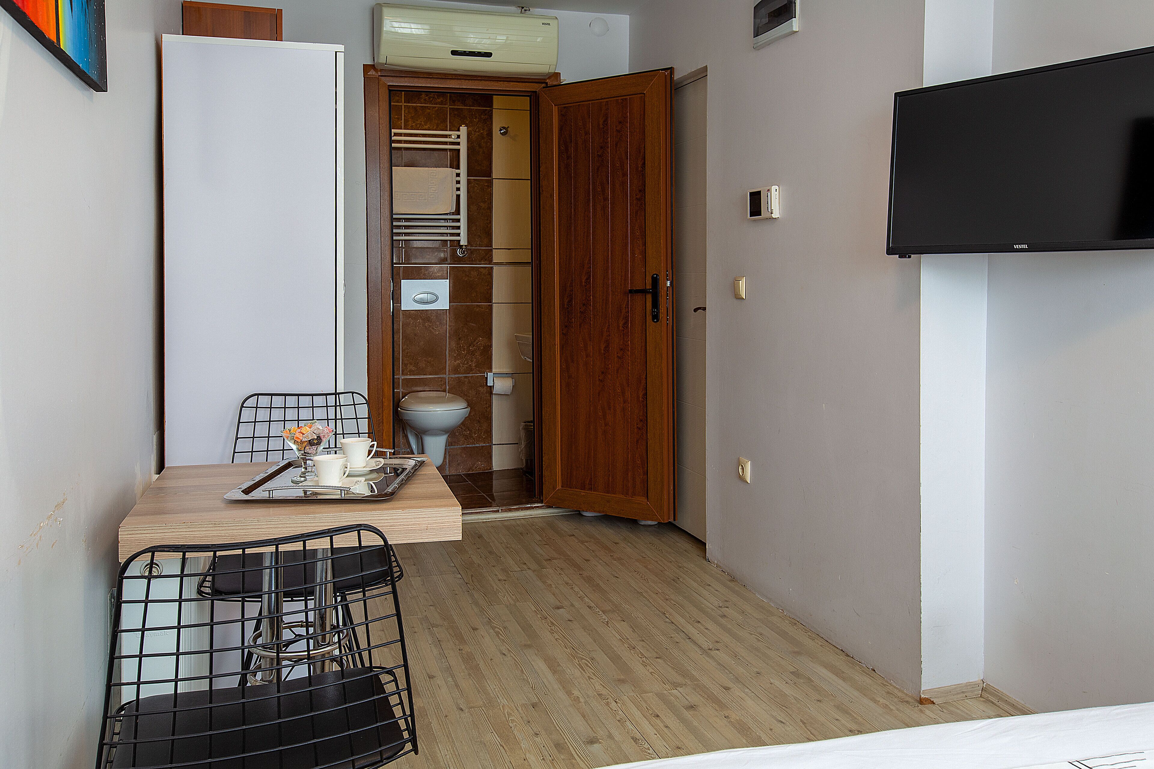 A compact room with a wooden dining table, chairs, a television, and a wardrobe.
