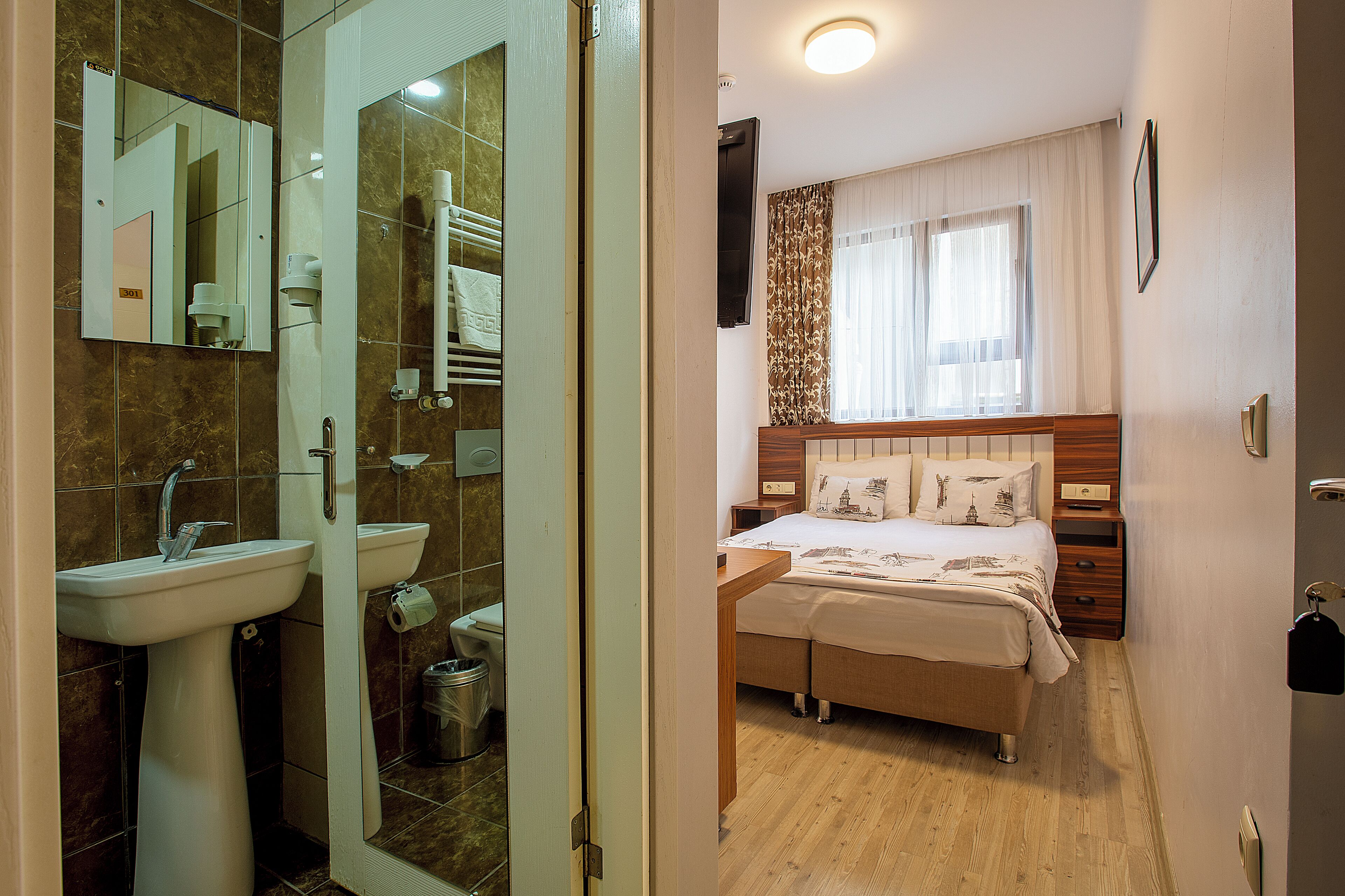 A hotel room with a bathroom, a bed with a wooden headboard, and a bedside table.