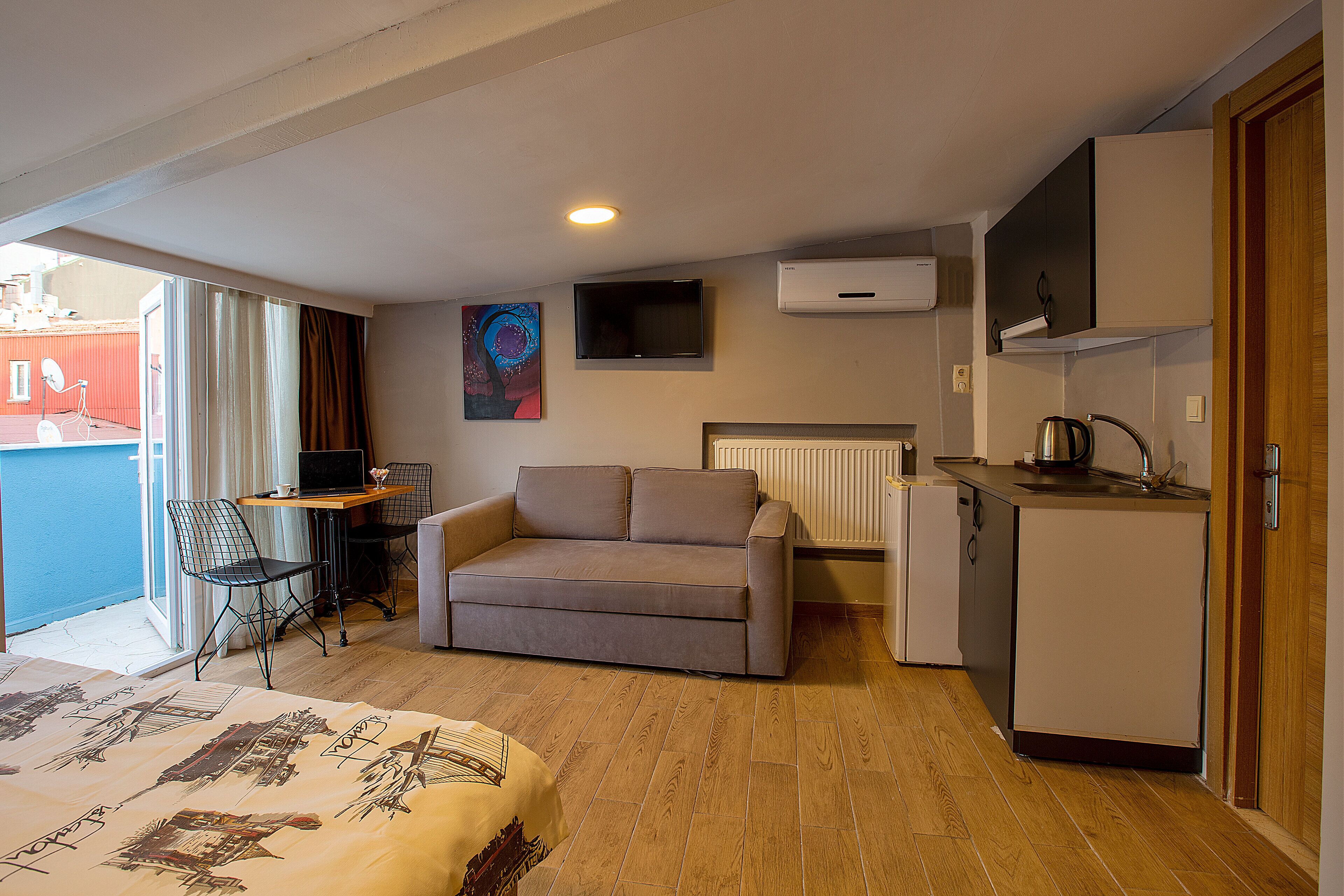 Une chambre d’hôtel compacte comprenant un canapé, une petite table à manger, une kitchenette et une grande fenêtre.