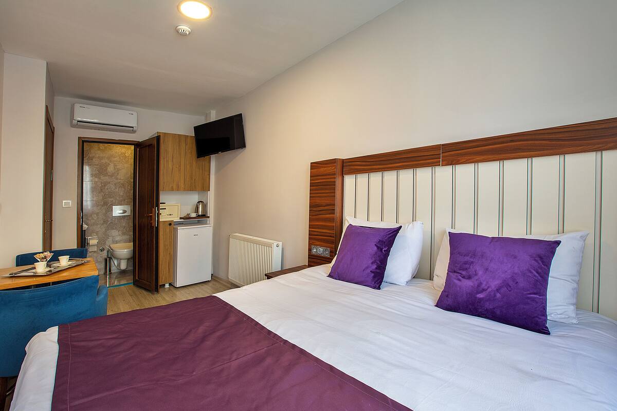 A hotel room with a bed, a desk, a television, and a kitchenette.