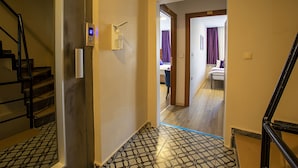Un corridoio d'albergo con pavimento a motivi decorativi, una sveglia digitale e un bagno con tenda viola.