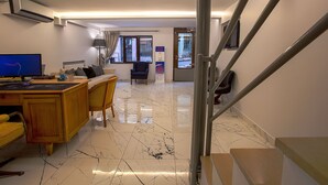 Una camera d'albergo moderna con una scrivania in legno, un computer, una sedia e un divano. Si nota una scala sullo sfondo.