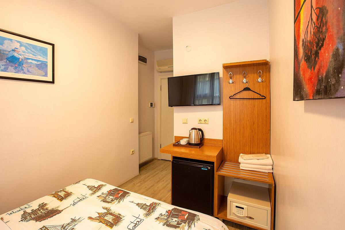 A hotel room with a bed, a desk with a coffee maker, a TV, and a painting on the wall.