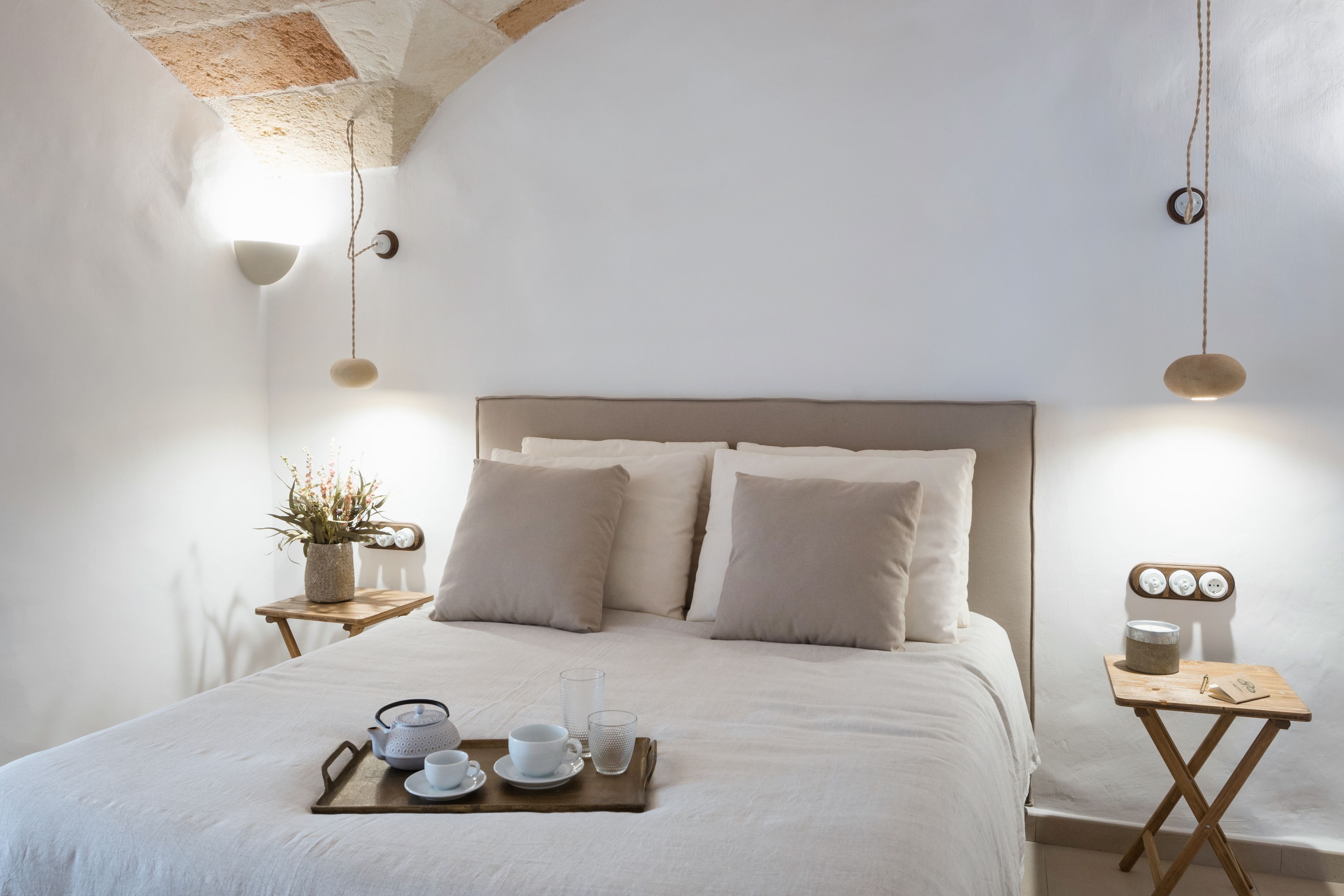 Un dormitorio ordenado con cama, mesitas de noche y una bandeja con tazas y tetera.