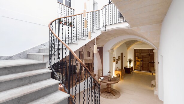 A grand staircase with a wrought iron railing and a round table with a vase in the middle of the room. - Hotel Nou Sant Antoni (Ciutadella de Menorca)