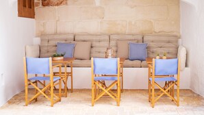 A cozy seating area with a stone wall backdrop, a cushioned bench with pillows, and wooden chairs. - Hotel Nou Sant Antoni (Ciutadella de Menorca)