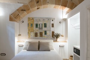 Un dormitorio con una cama, un cuadro de un edificio, una planta en maceta y una ventana con un tendedero.