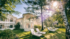 A large house with a porch, a lawn with sun loungers, and a birch tree. - ROEWERS Privathotel & Spa (Sellin)