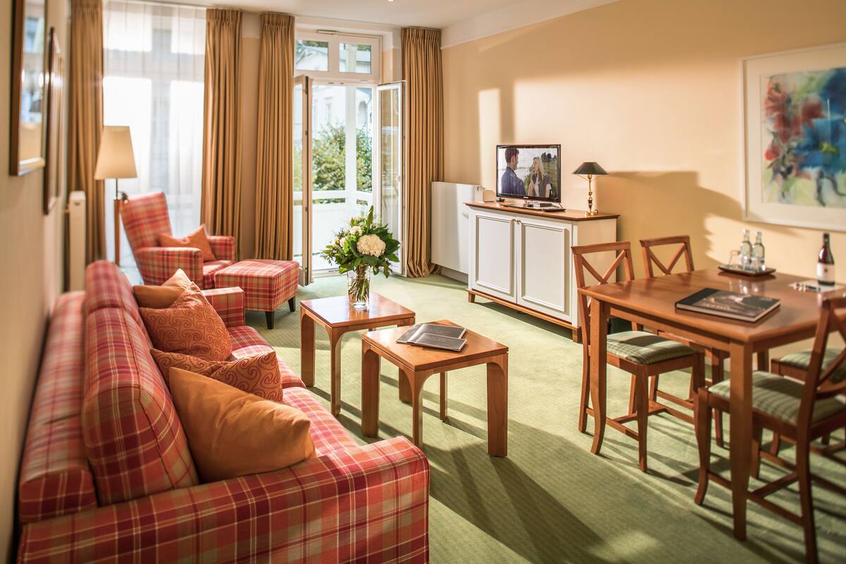A hotel room with a plaid sofa, a dining table with chairs, a TV, and a cabinet.