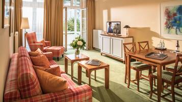 A hotel room with a plaid sofa, a dining table with chairs, a TV, and a cabinet.